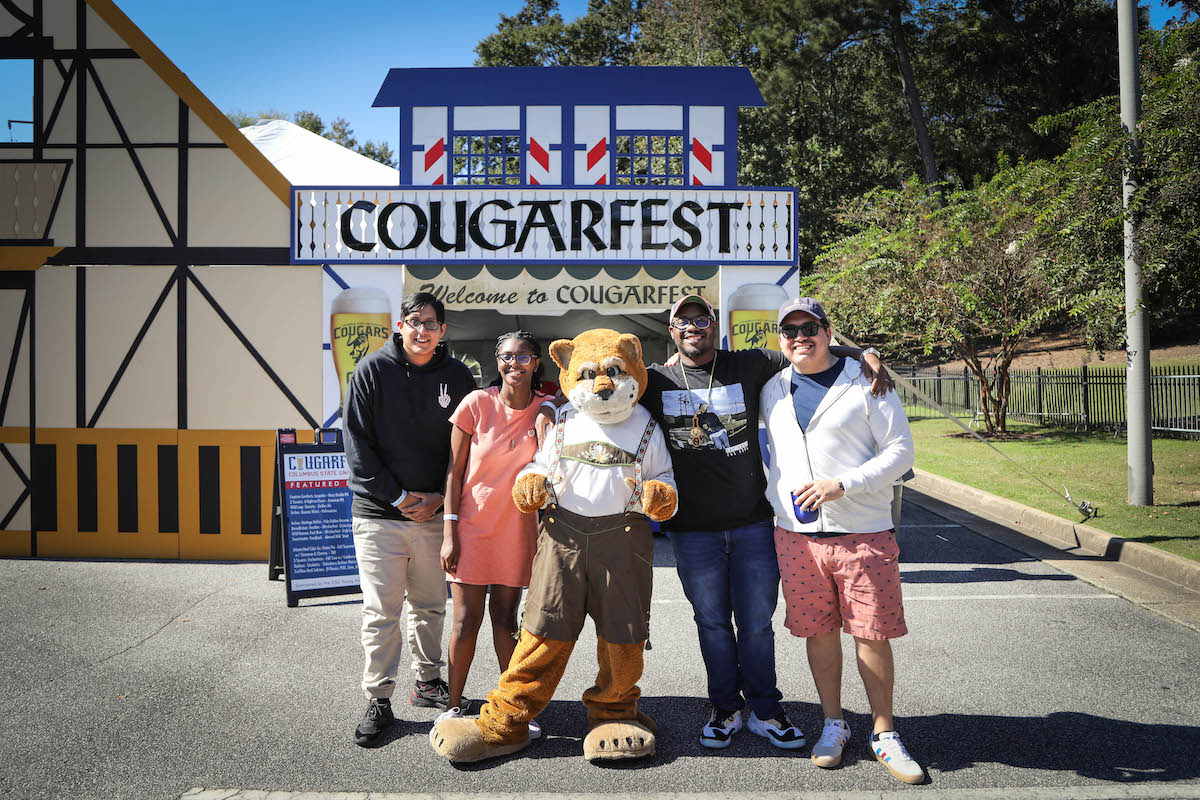 Several students and Cody the Cougar (mascot) in front of 'Welcome to CougarFest' decorations