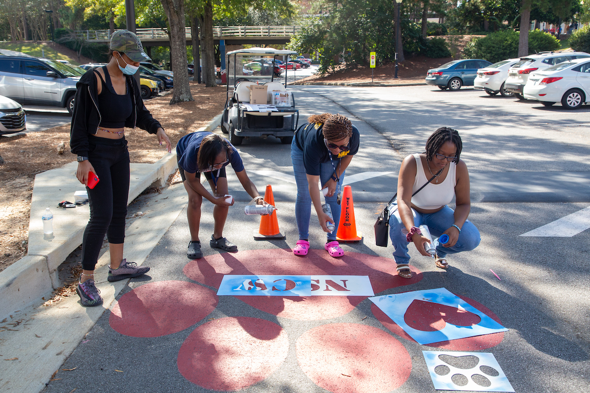 Several students stenciling the sidewalk with homecoming art